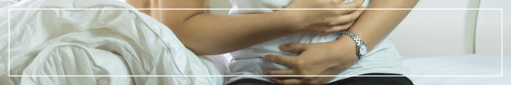 woman holding stomach in pain sat on her bed